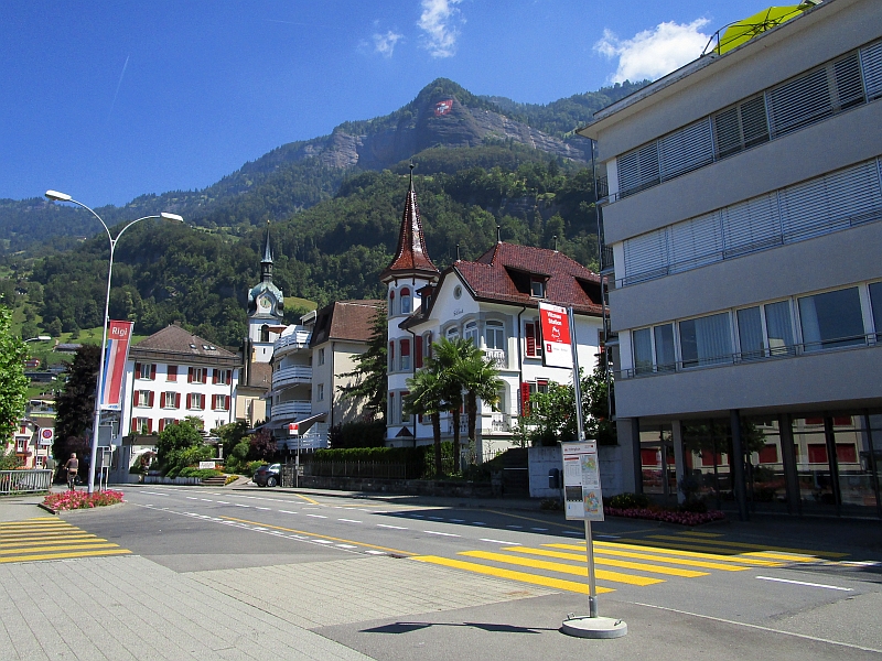Schweizerfahne über den Dächern von Vitznau, im Vordergrund die Bushaltestelle
