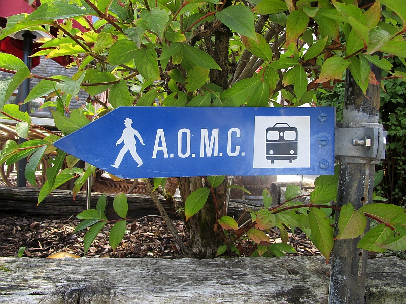 Wegweiser mit Hinweis auf die frühere Aigle-Ollon-Monthey-Champéry-Bahn (AOMC)